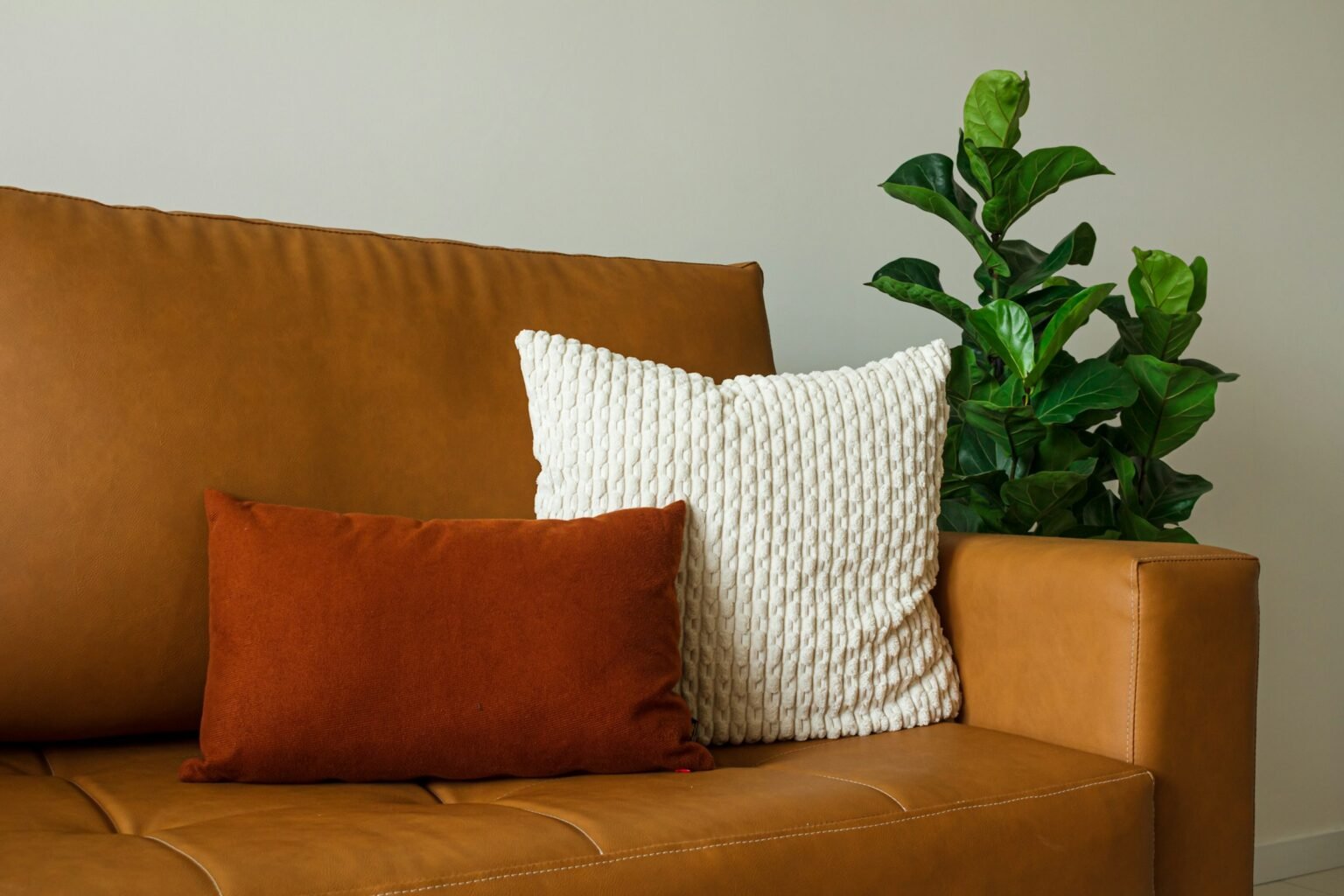 Burnt orange pillows for couch styling: a rust lumbar pillow and cream knit pillow on a tan leather sofa