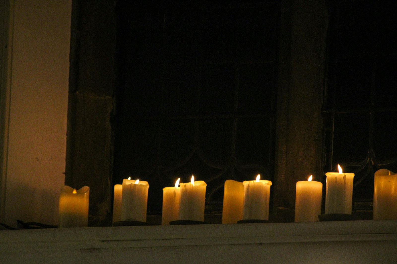 A row of lit white candles glowing on a window ledge at night, the classic Christmas window candles look