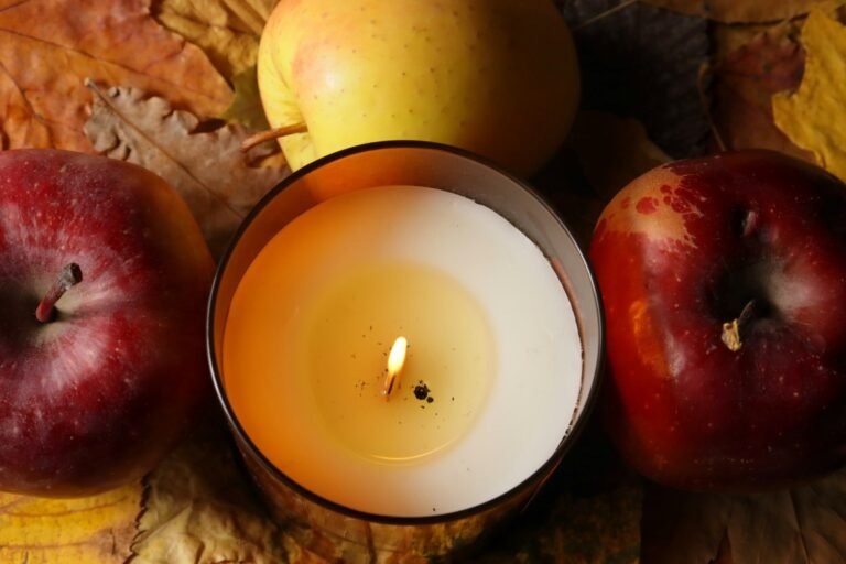 Cinnamon apple candle mood: a lit jar candle between red and yellow apples on autumn leaves