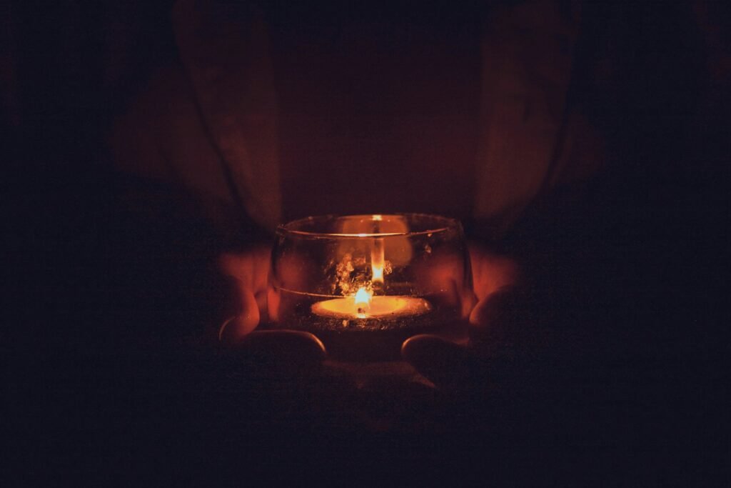 Hands holding a glass jar candle, the kind an electric lighter for candles reaches with an angled tip
