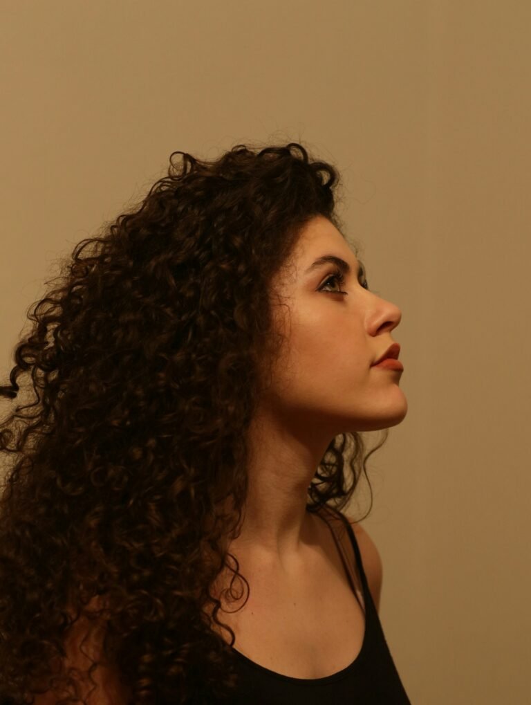 Daily Dose leave in conditioner review: woman with long, defined dark curls in profile against a warm beige wall