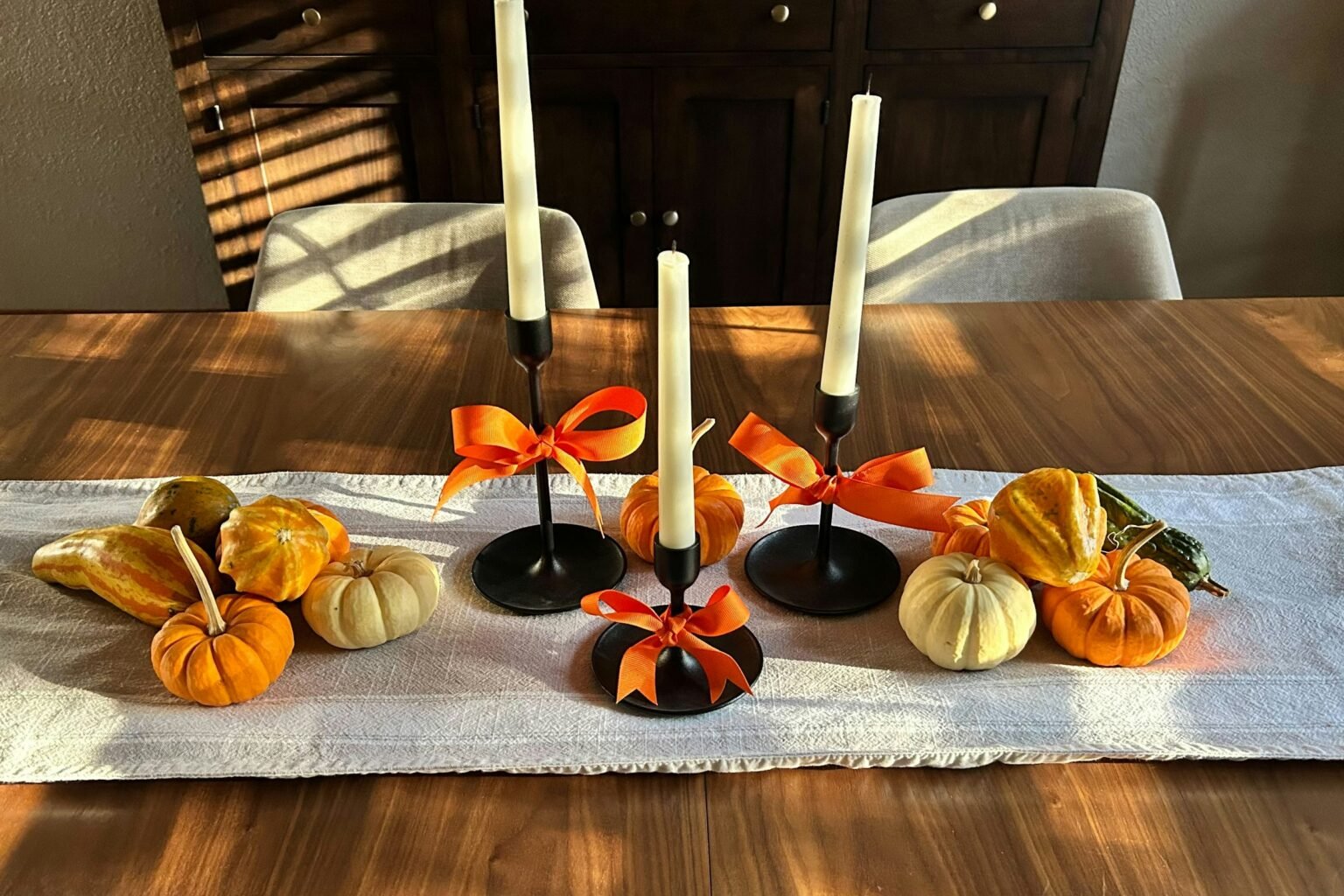 Fake mini pumpkins and gourds on a linen table runner with tall candlesticks