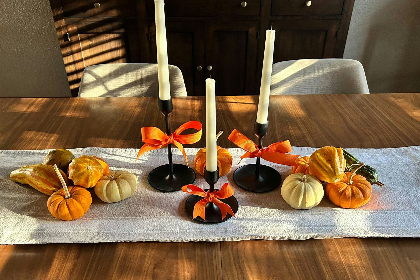 Fake mini pumpkins and gourds on a linen table runner with tall candlesticks