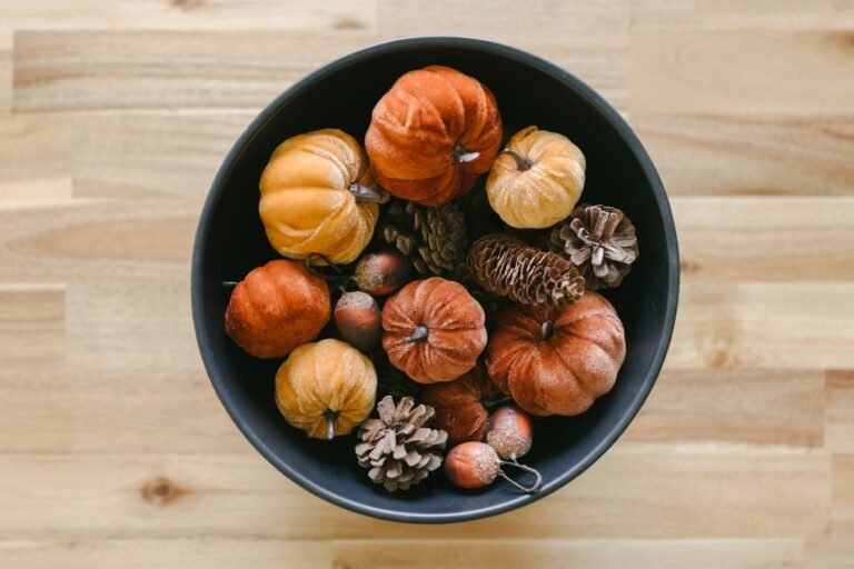 Fall bowl filler idea: a dark bowl filled with mini pumpkins and pinecones on a wood table