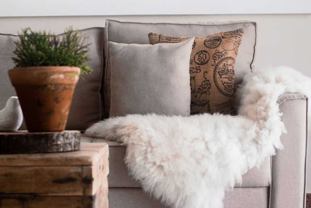 White shaggy faux fur throw draped over the arm of a gray sofa with linen pillows, an easy way to style an oversized faux fur throw blanket