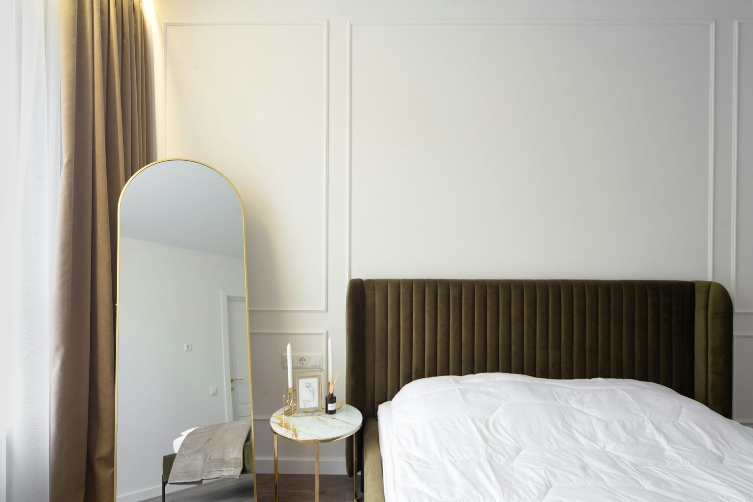 Full length floor mirror styling: a gold arched mirror beside a velvet bed and a small side table