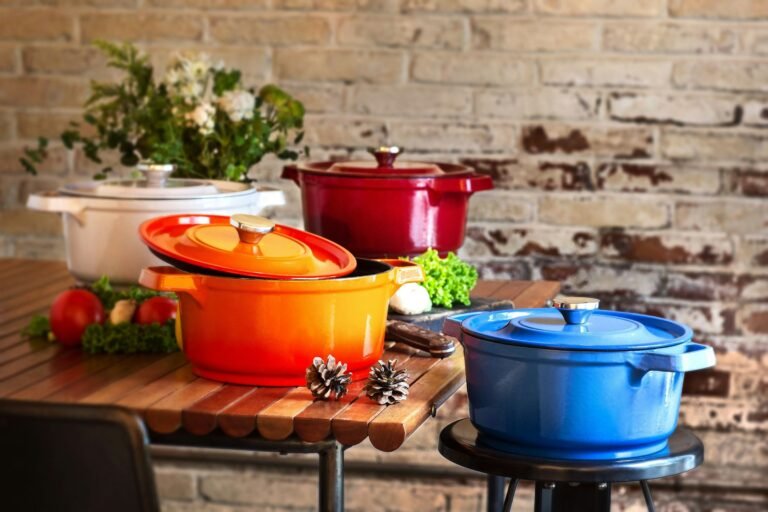 Le Creuset vs Staub: colorful enameled cast iron Dutch ovens in white, orange, red and blue on a rustic wooden table