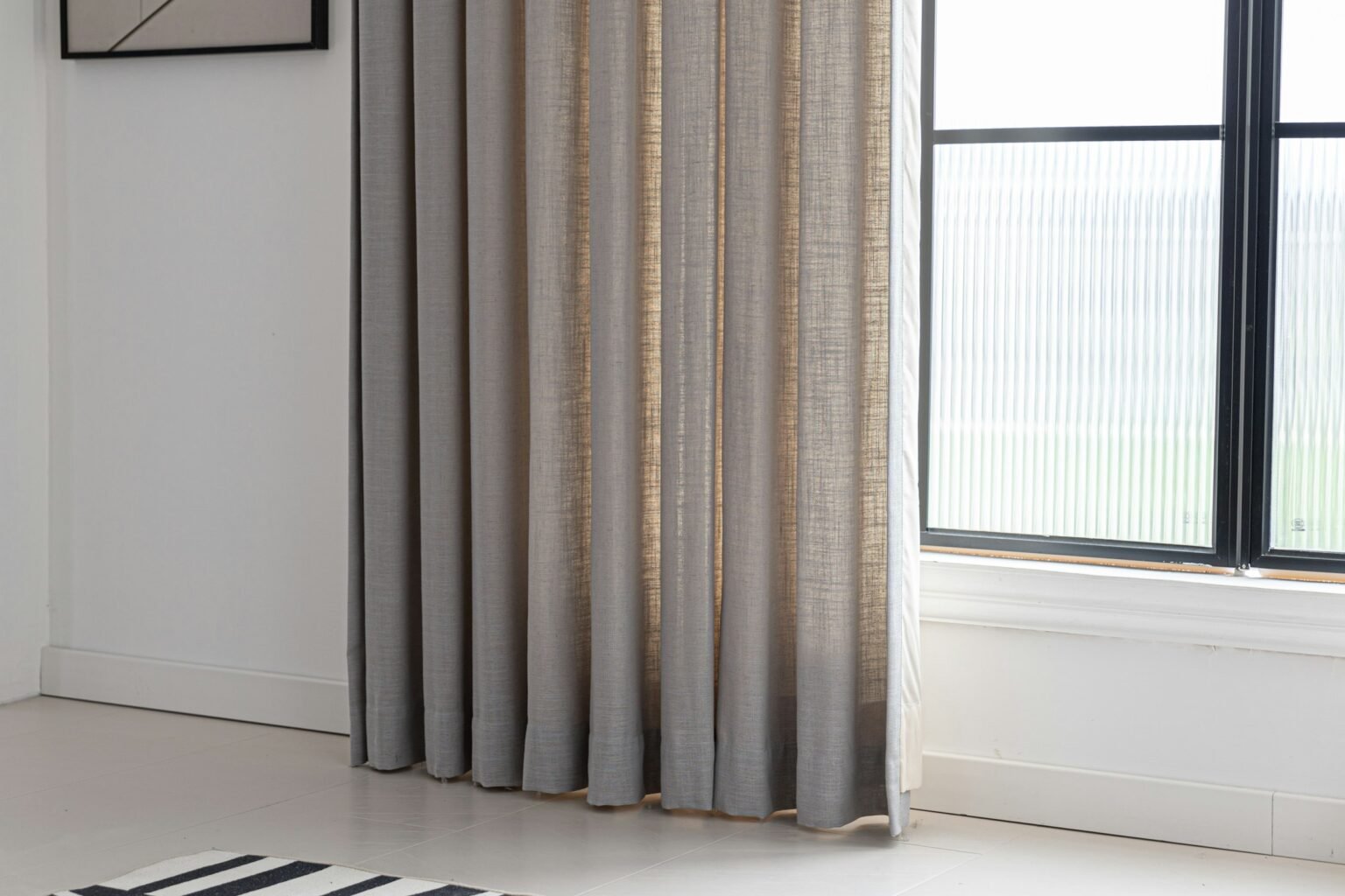 Linen blackout curtains in a textured natural tone hanging beside a bright black-framed window