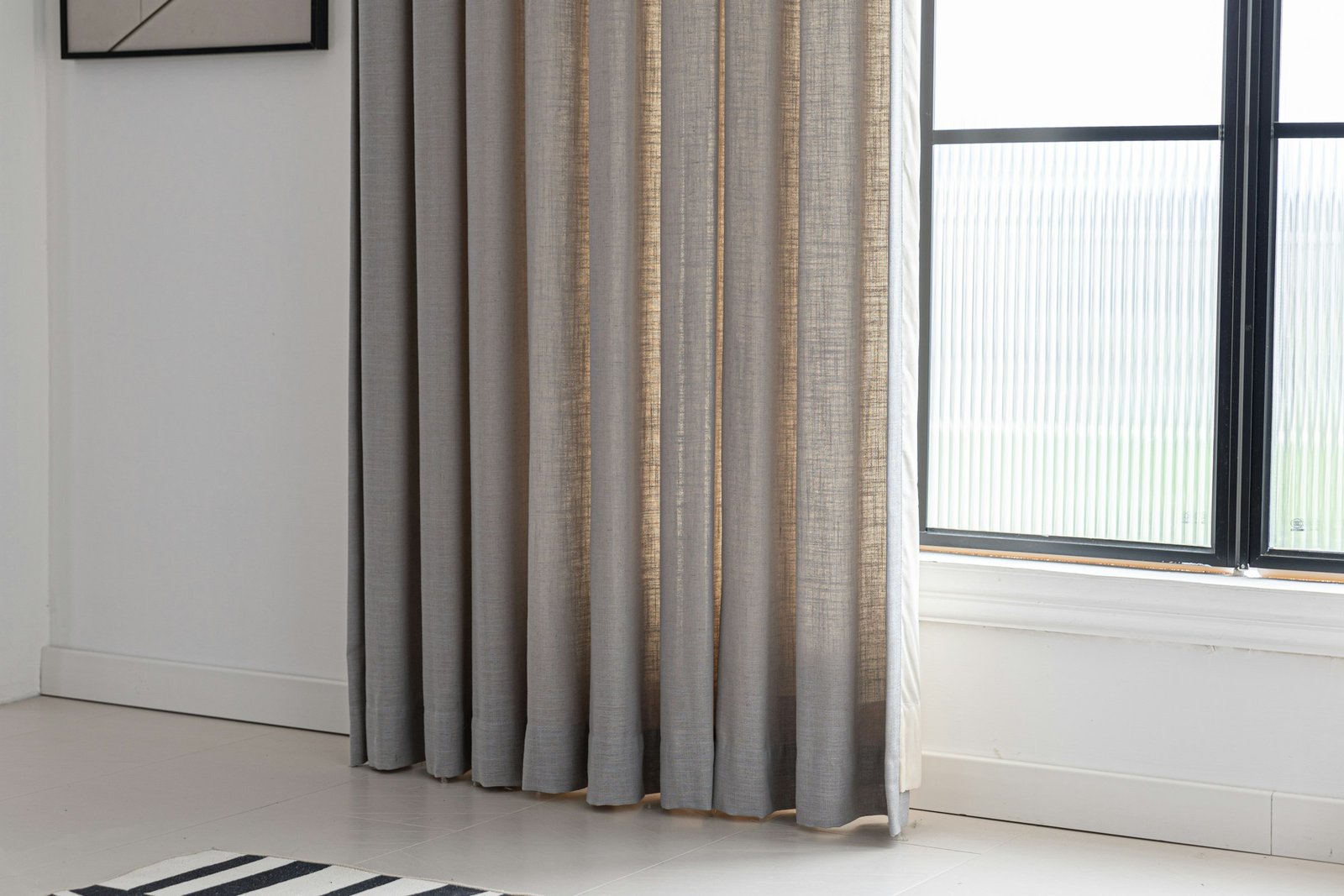 Linen blackout curtains in a textured natural tone hanging beside a bright black-framed window