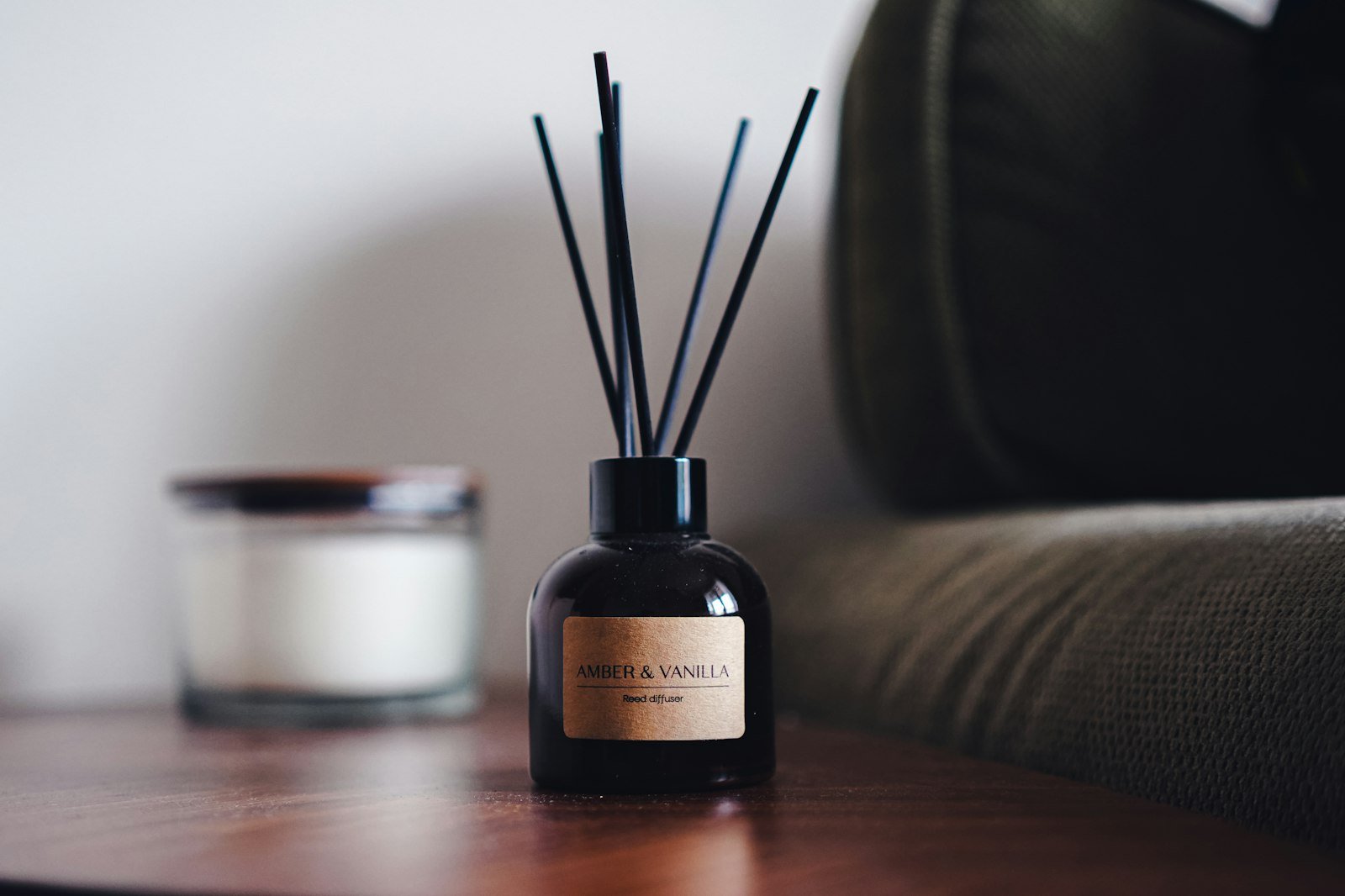 Luxury home fragrance gifts: a dark glass reed diffuser and a scented candle on a wooden side table