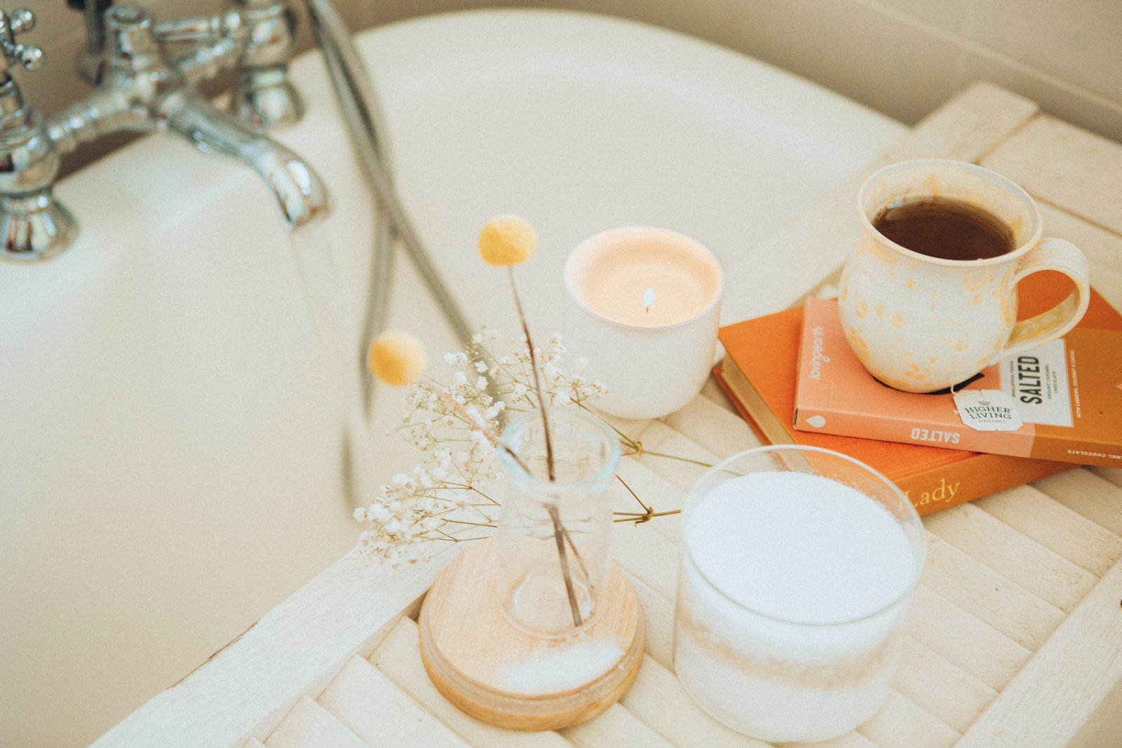 Luxury self care gifts for a night in: a bath tray with a candle, tea, books and bath salts by the tub