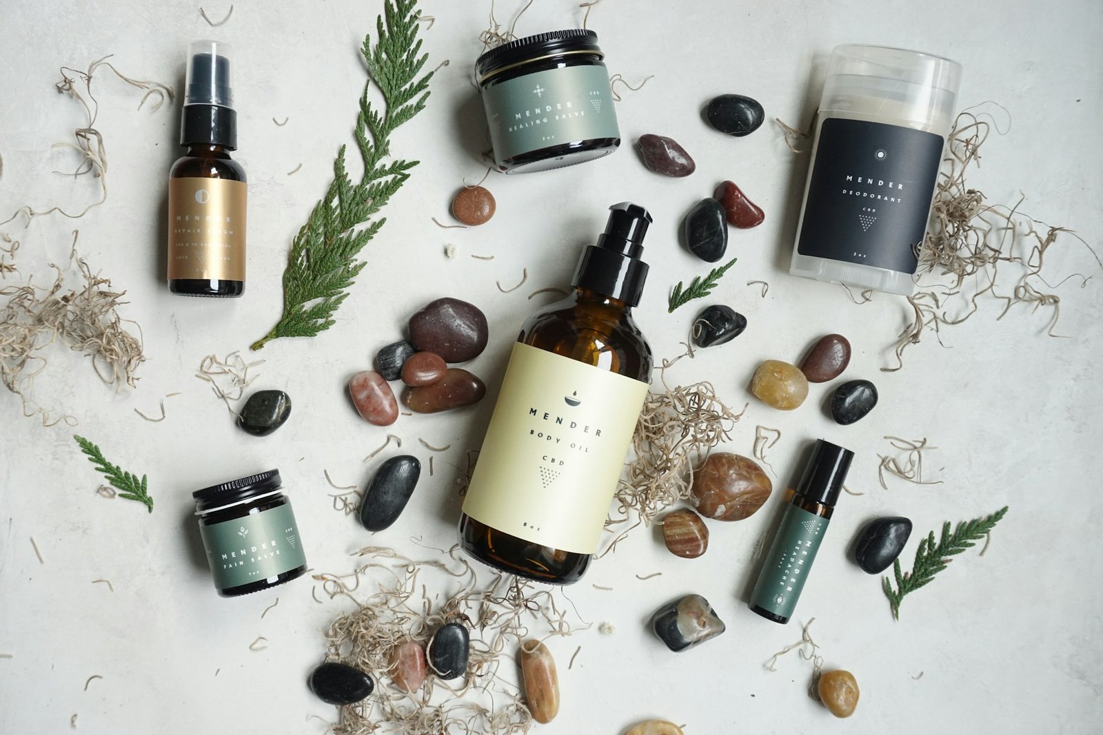 Luxury skincare gift sets: serum, body oil and cream jars laid out with evergreen sprigs and smooth stones