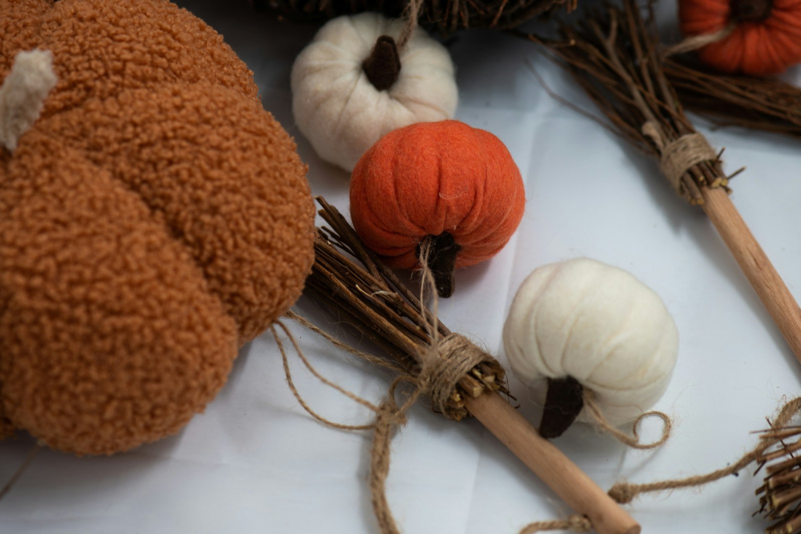 Mini knit pumpkins idea: soft orange and cream textured pumpkins grouped with tiny twig brooms on a bright white table