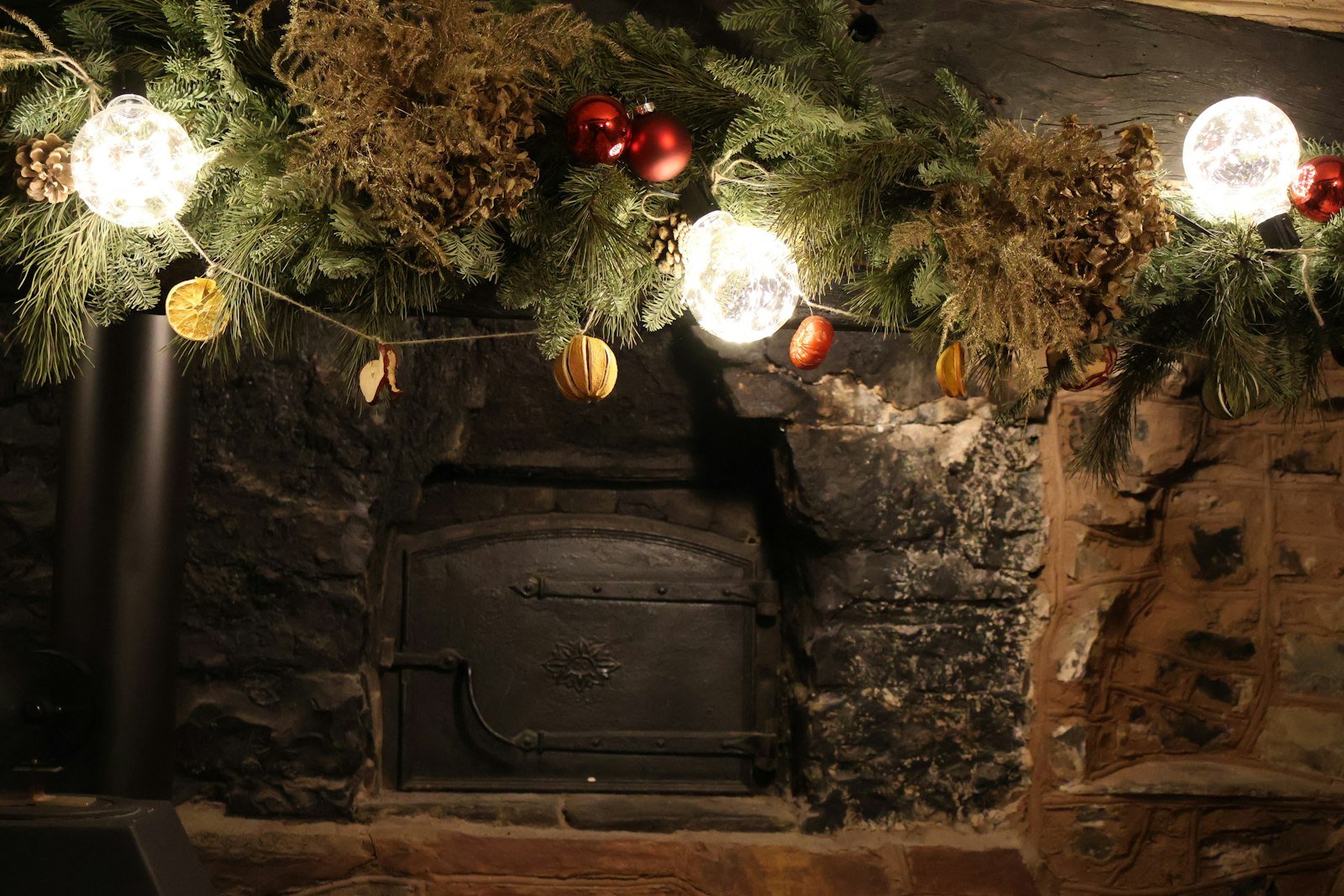 Norfolk pine garland idea: lush evergreen garland with globe lights and red ornaments across a rustic stone fireplace mantel