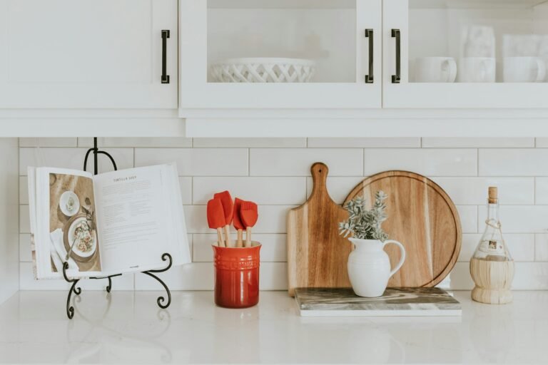 Personalized recipe box gift idea: a bright white kitchen counter with an open cookbook on a stand, wooden cutting boards and utensils