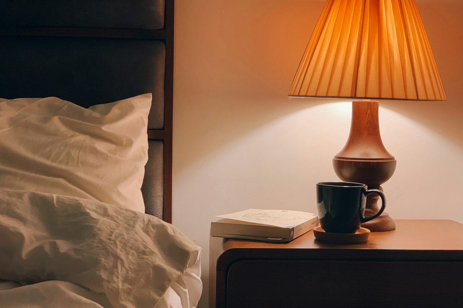 Sunrise alarm clock mood: a warm bedside lamp glowing on a wooden nightstand