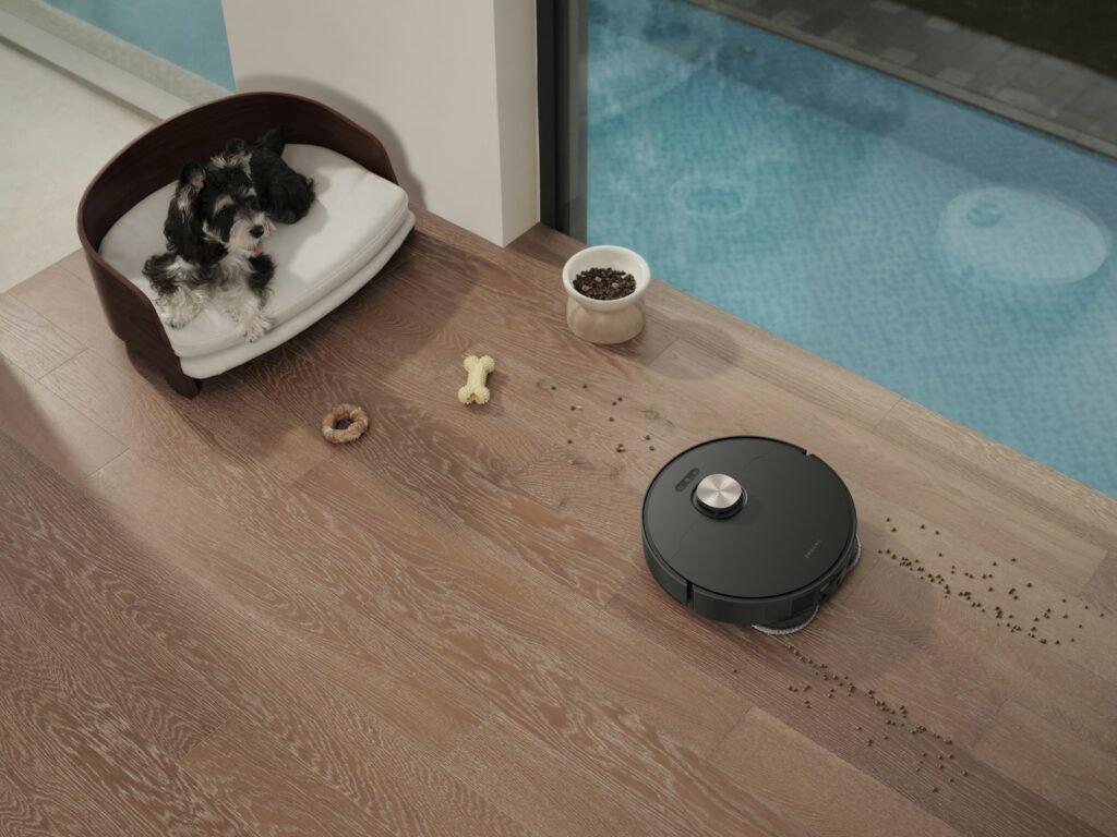 Roomba vs Roborock for pet hair: a dark robot vacuum picking up spilled kibble near a dog bed on hardwood