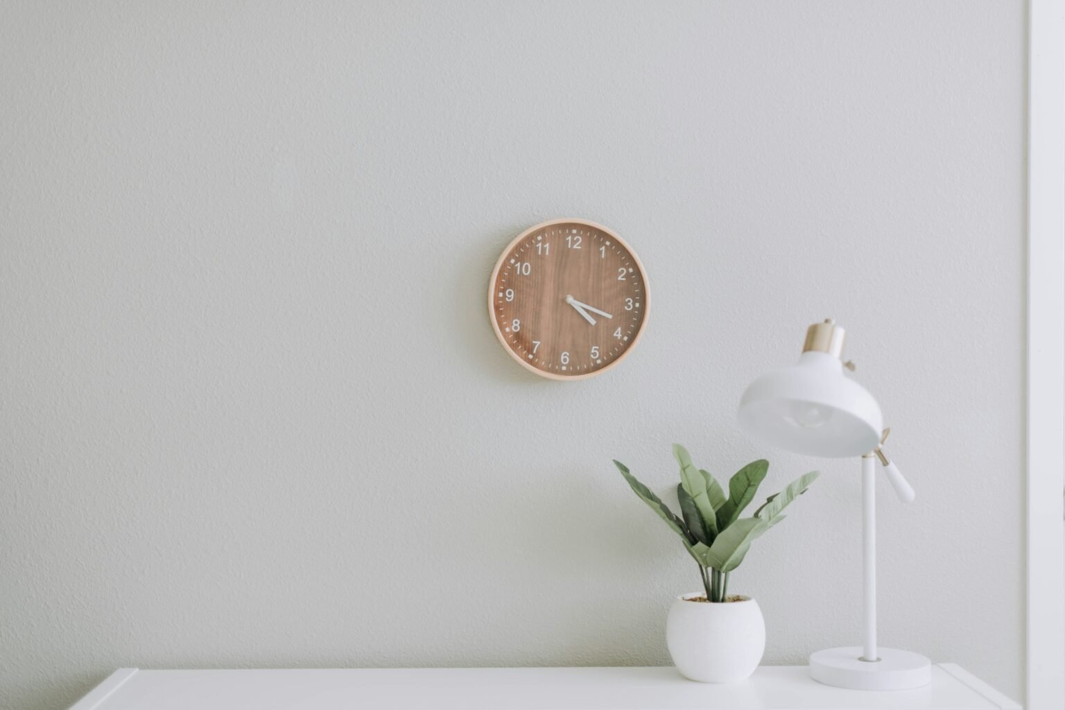 Silent wall clock idea: a small round clock above a white desk with a lamp and plant