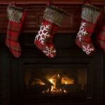 Stocking stuffers for men: red plaid Christmas stockings hanging over a lit fireplace