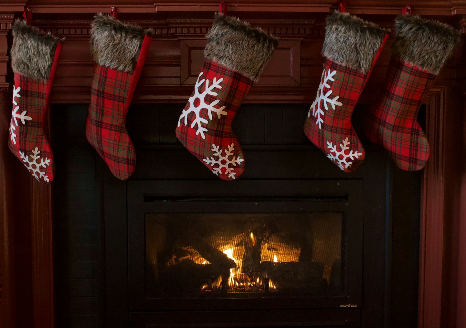 Stocking stuffers for men: red plaid Christmas stockings hanging over a lit fireplace