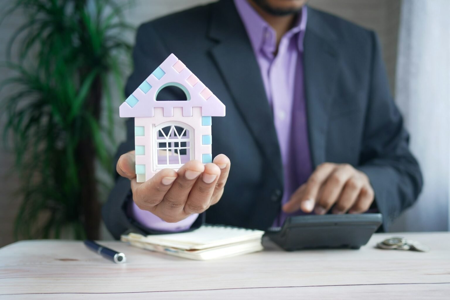 Mortgage payment calculator – Man holding a model house at a desk with a calculator