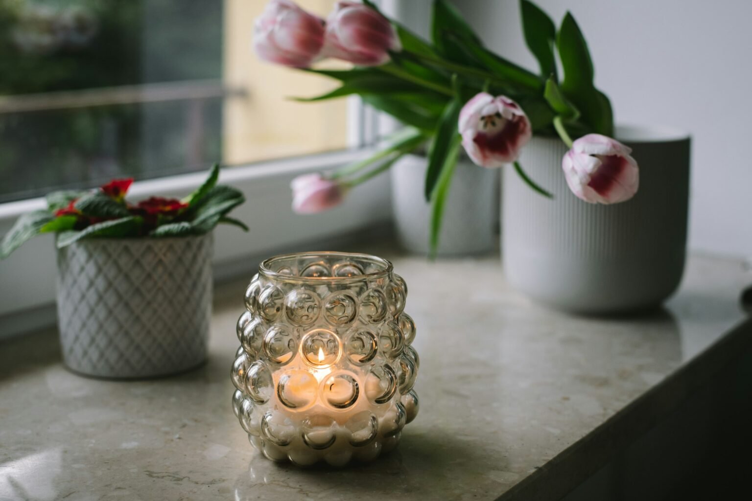 Tea light candle decoration ideas: a glass tealight holder glowing on a bright windowsill with tulips