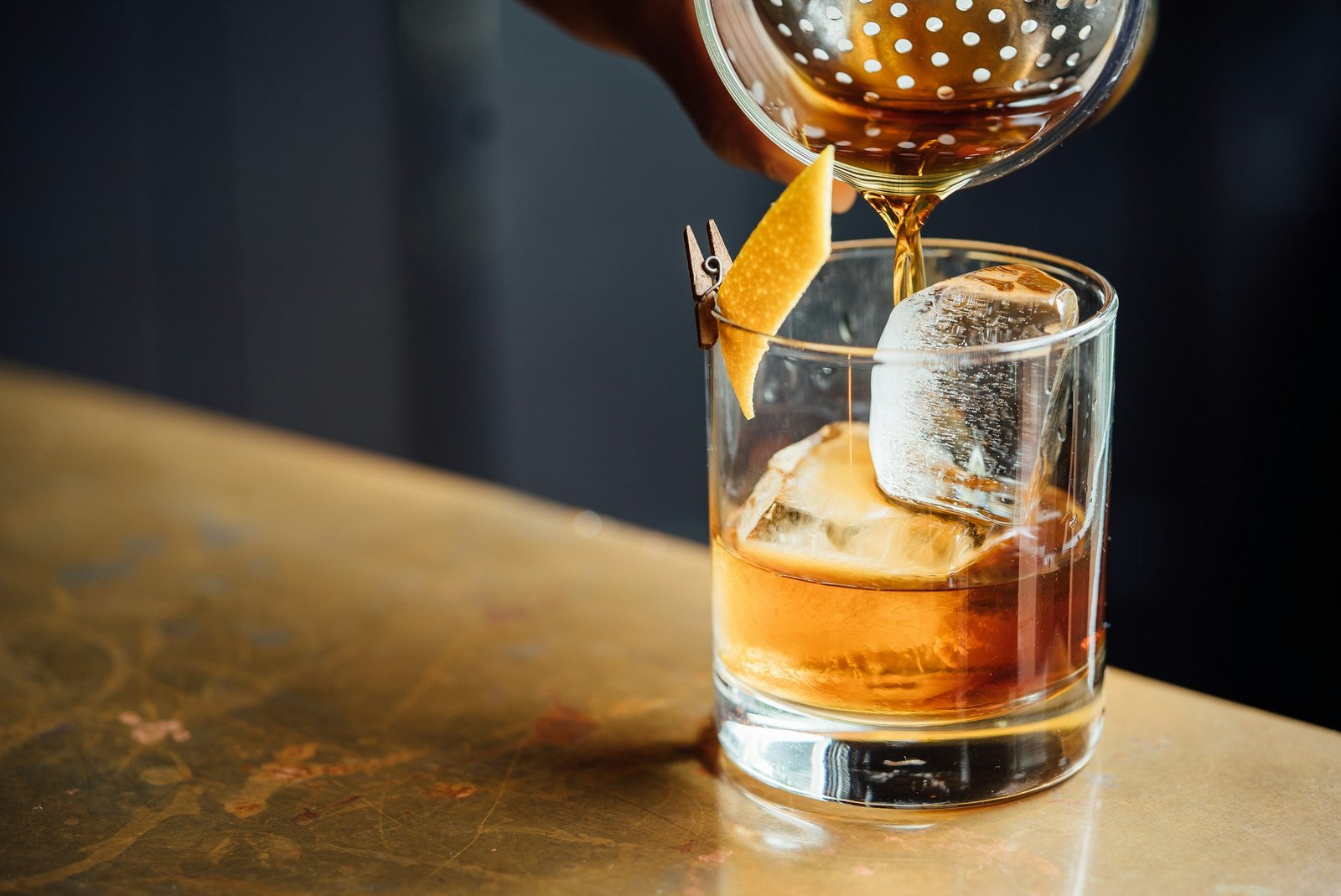 Whiskey smoker kit gift idea: bourbon poured over a large ice cube in an old fashioned glass with an orange peel