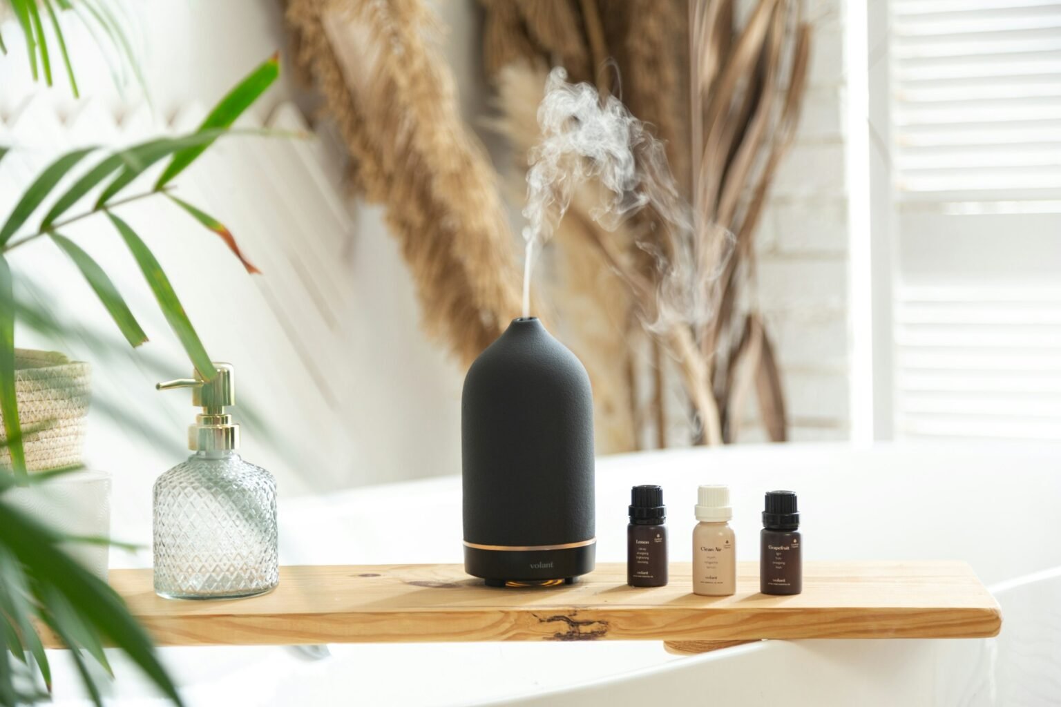 White tea diffuser oil idea: a matte black ultrasonic diffuser misting beside small oil bottles on a bright bath shelf